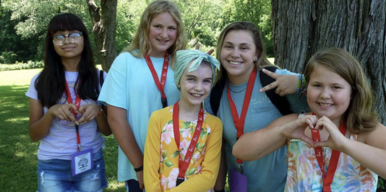A group of young girls smiling and making heart and peace gestures with their hands